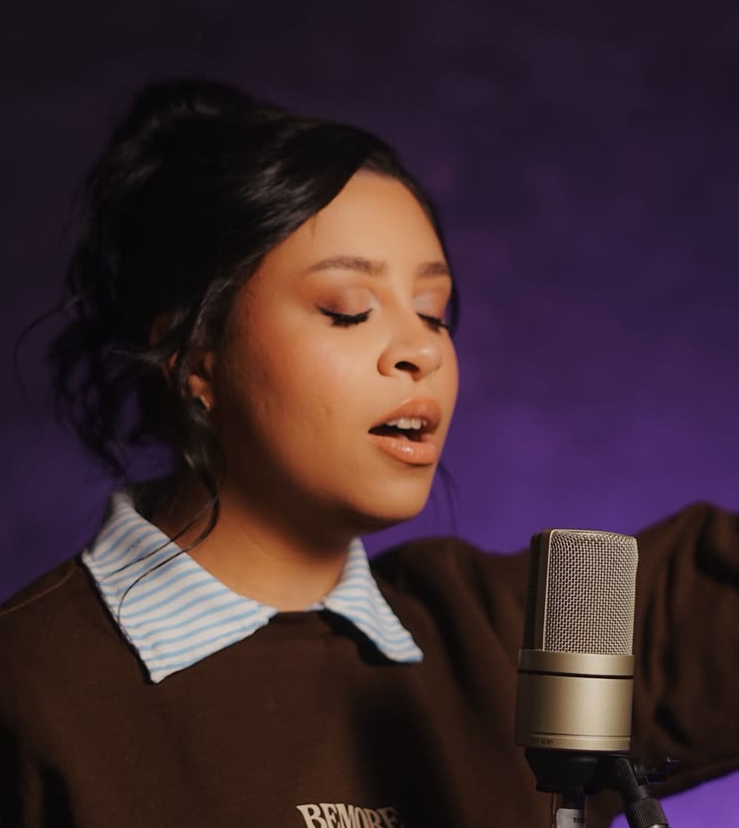 Vanessa da Luz de olhos fechados, cantando diante de um microfone, com fundo roxo